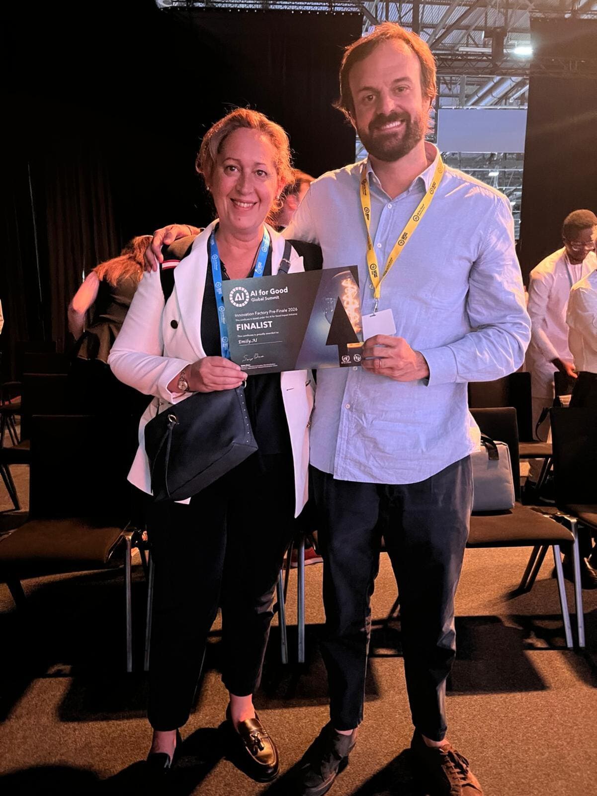 La Dra. Sara Heili y Daniel Oliva sostienen el diploma de finalista en el AI for Good Global Summit 2026 para Emily.AI